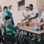 A Group of Volunteers Assisting an Elderly Person on a Black Wheelchair For Charity
